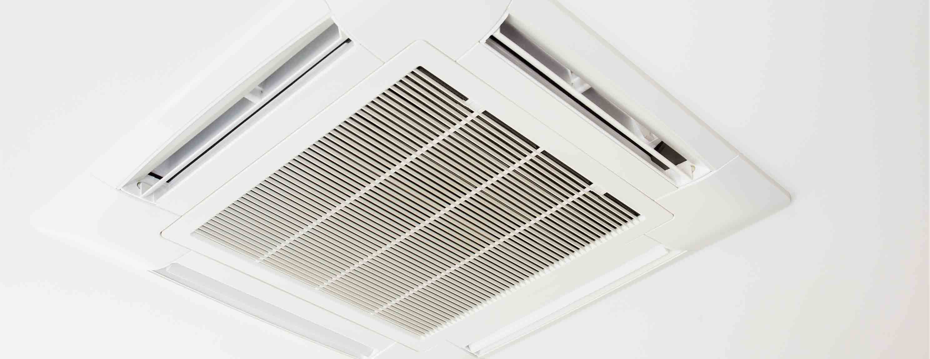 Eine weiße, rechteckige Klimaanlage ist an der Decke installiert. Sie hat Lüftungsschlitze und passt sich in einem minimalistischen, modernen Raum ein.