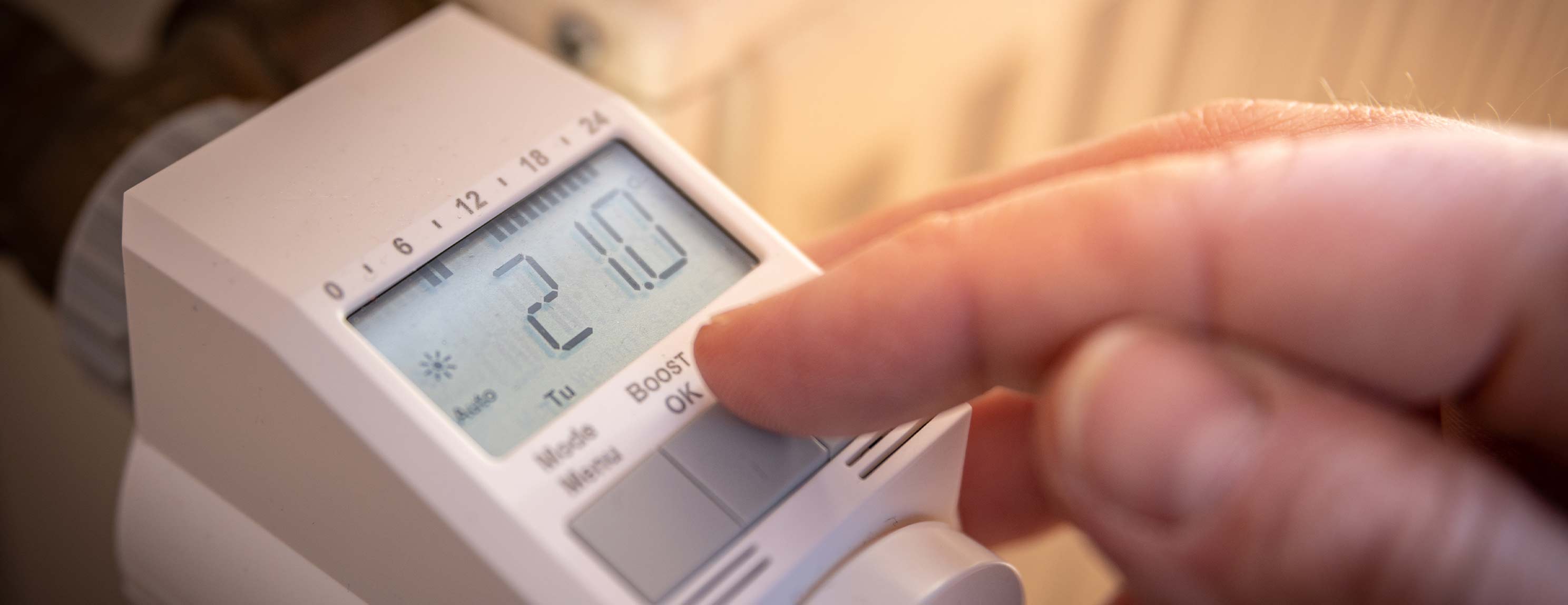 Ein digitaler Heizkörperthermostat zeigt 21,0 Grad Celsius an. Eine Hand drückt eine Taste. Der Hintergrund ist unscharf.